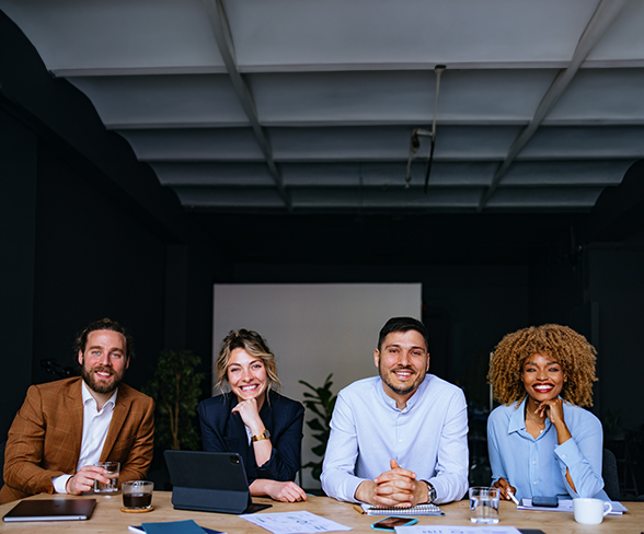 Portrait Of Happy Businesspeople Sitting In A Row At Office Desk