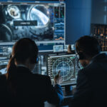 Group of People in Mission Control Center Establish Successful Video Connection on a Big Screen with an Astronaut on Board of a Space Station. Flight Control Scientists Sit in Front Computer Displays.